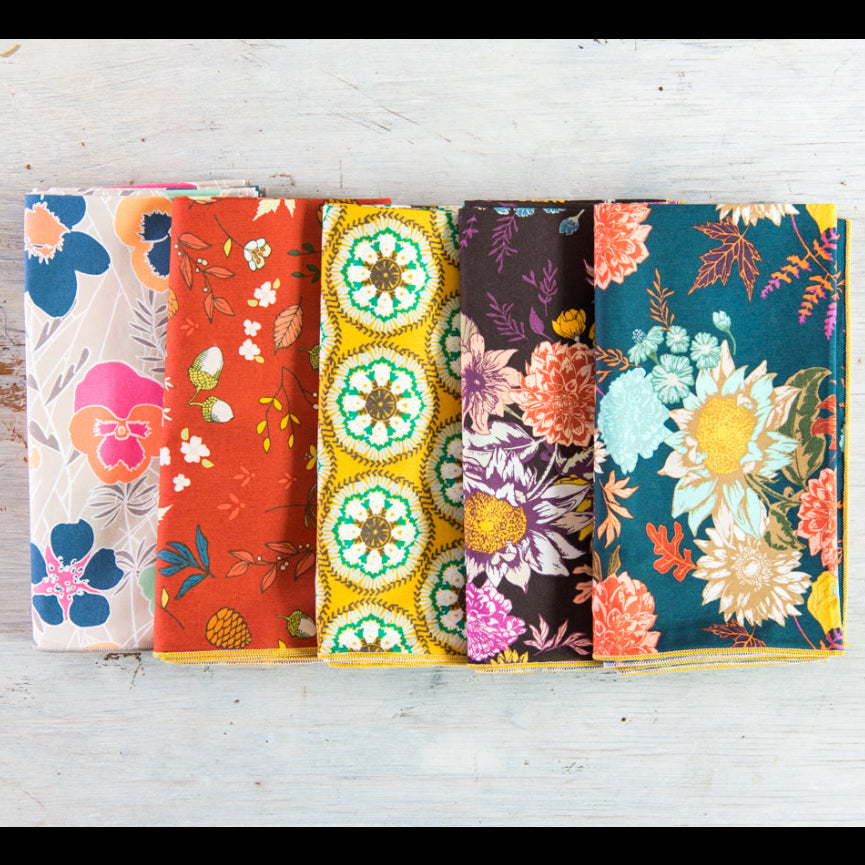 Five colorful fabric swatches with floral patterns arranged on a light wooden surface.