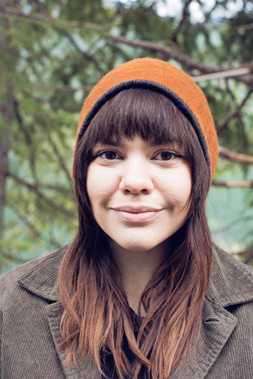 Person wearing an orange beanie and brown coat with a blurred natural background