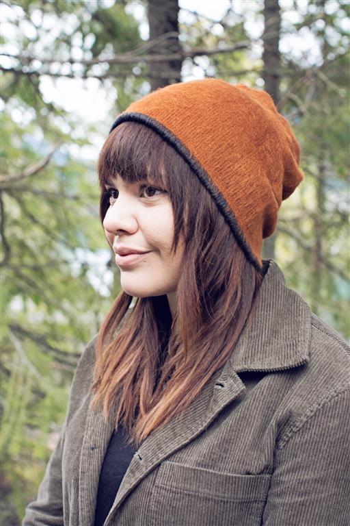 Woman wearing an orange beanie and brown coat in a forest setting