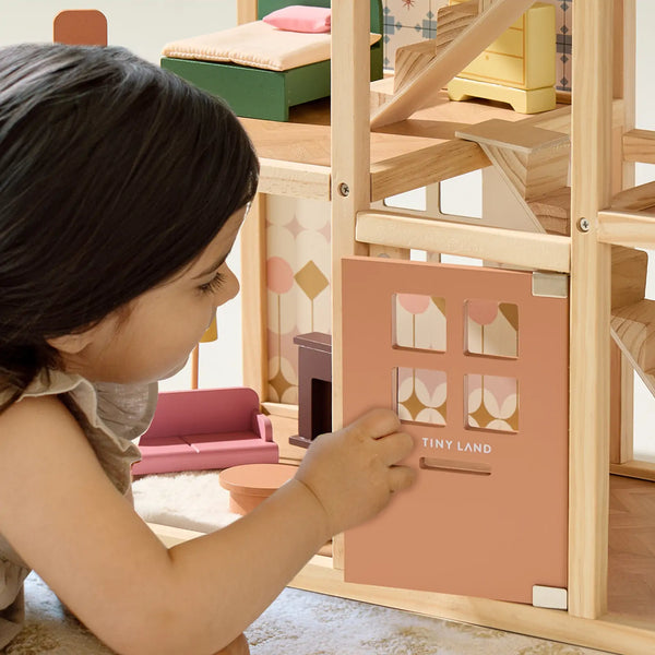 Child playing with a wooden dollhouse and pink door