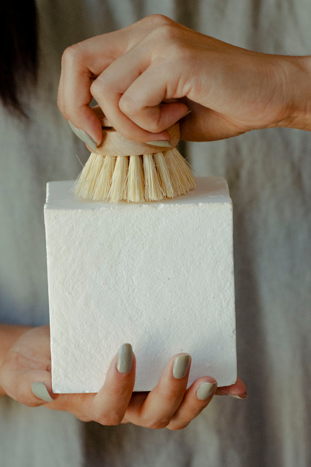 Person holding a white block with a natural bristle brush on top against a neutral background