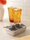 Metal ice cube tray on a kitchen counter with two amber glasses in the background.