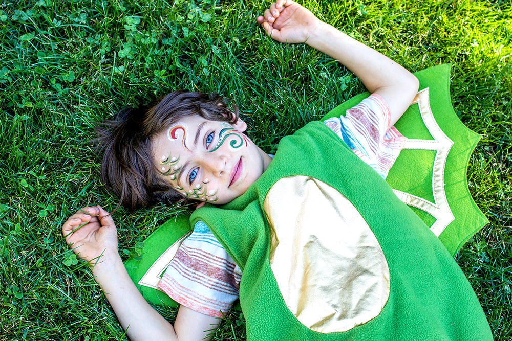 Child in a green dinosaur costume lying on grass