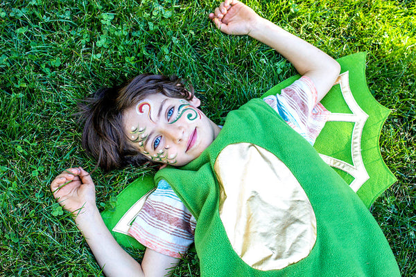 Child in a green dinosaur costume lying on grass