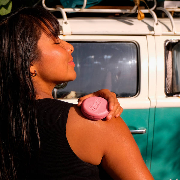 Woman applying sunscreen on her shoulder with a vintage van in the background