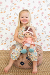 Flatlay of Earthtone Floral Tie Shoulder Jumpsuit with Paloma doll and coordinating organic muslin doll clothes accessories