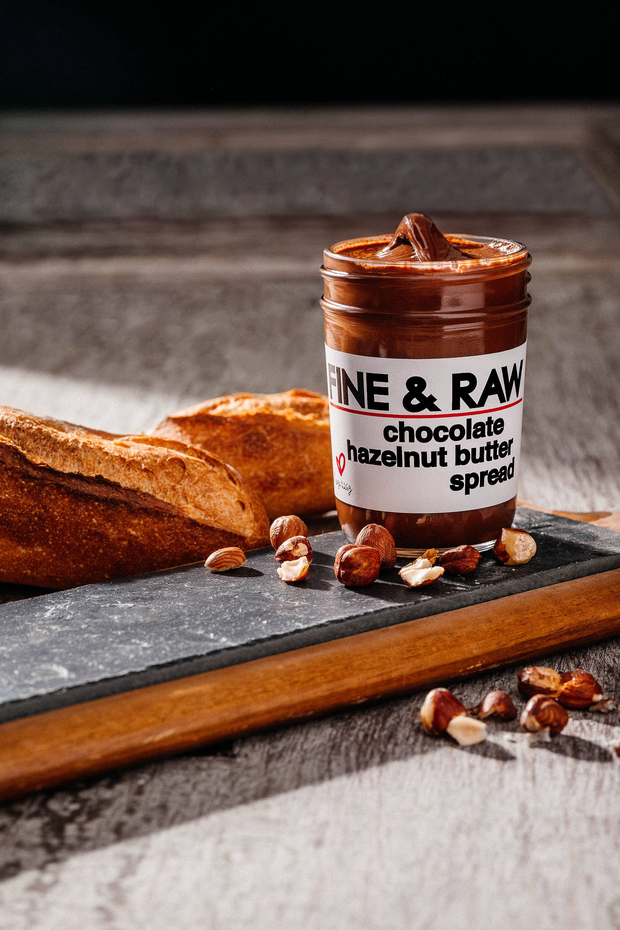 Jar of chocolate hazelnut butter spread on a wooden board with bread and nuts.