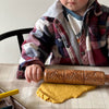 Child rolling yellow dough with a wooden rolling pin on a kitchen counter.