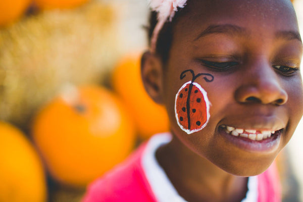 Child with a ladybug face paint in front of pumpkins