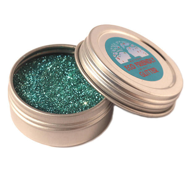 Open container of green glitter with a label on a white background