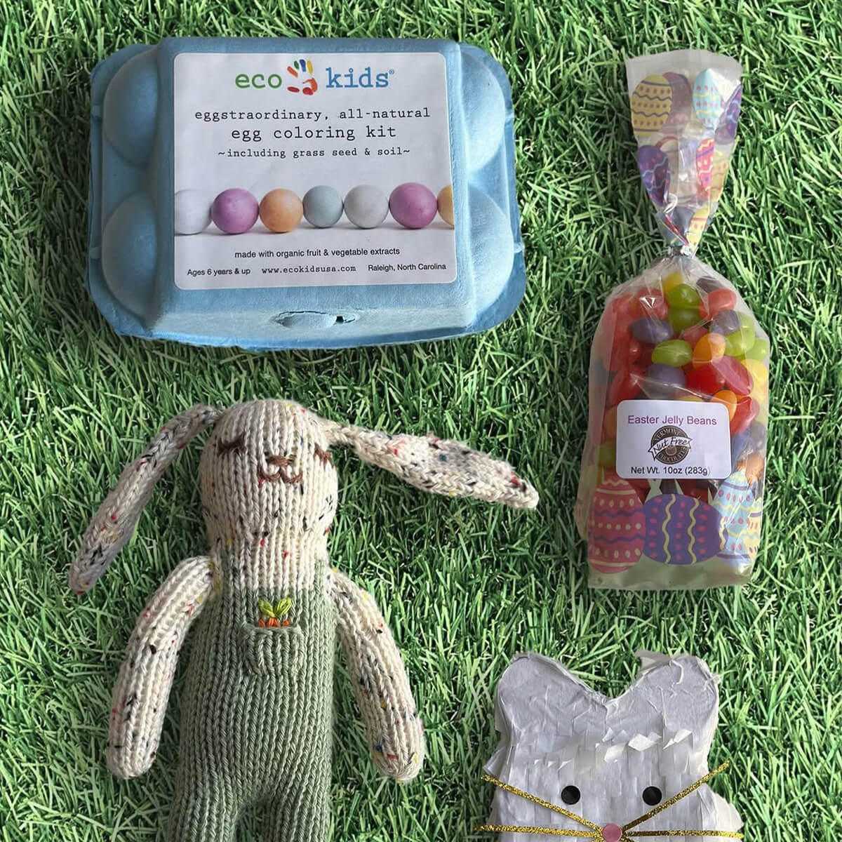 Easter-themed items including an egg coloring kit, knitted bunny, and candy on grass