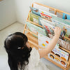 Young child independently reaching for a book on the Elena Kids front-facing Montessori bookshelf