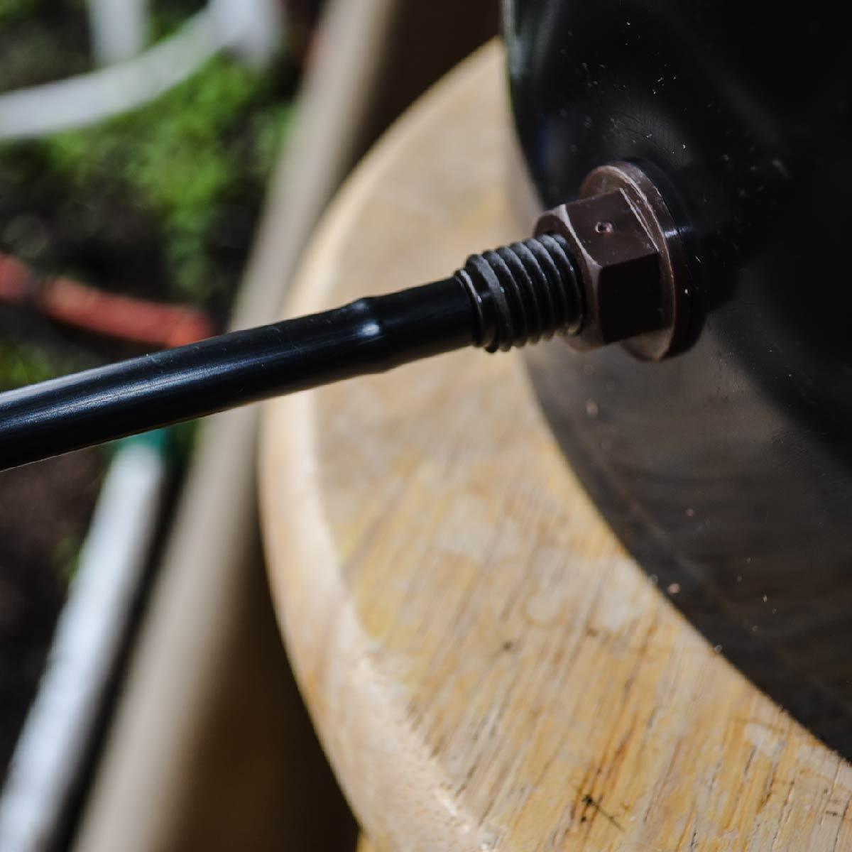 Close-up of a black metal rod with a nut attached to a wooden surface.