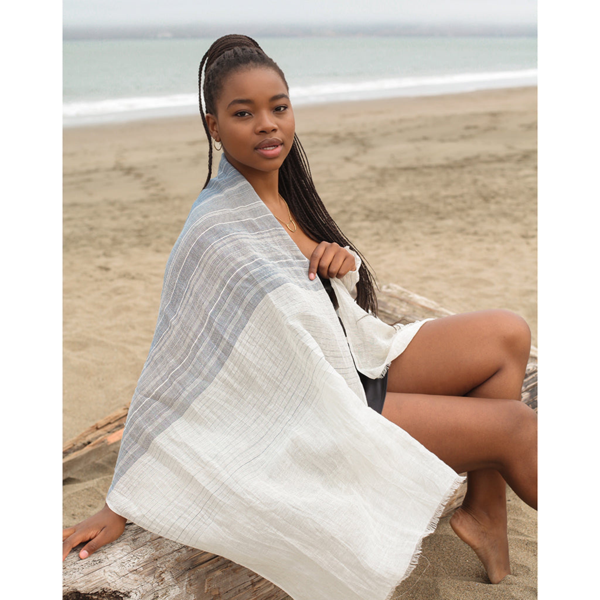 Woman sitting on a beach with a white and gray striped line scarf