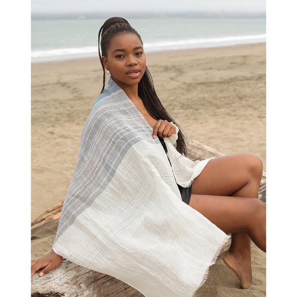 Woman sitting on a beach with a white and gray striped line scarf
