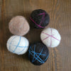 Five felted balls with yarn patterns on a wooden surface