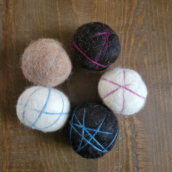 Five felted balls with yarn patterns on a wooden surface