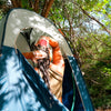 Person washing hair inside a tent in a forest setting