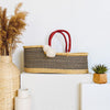 Woven basket with striped pattern and red handles on a white surface, surrounded by decorative items.
