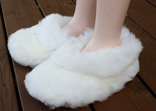 White fluffy slippers worn by a person on a wooden floor.