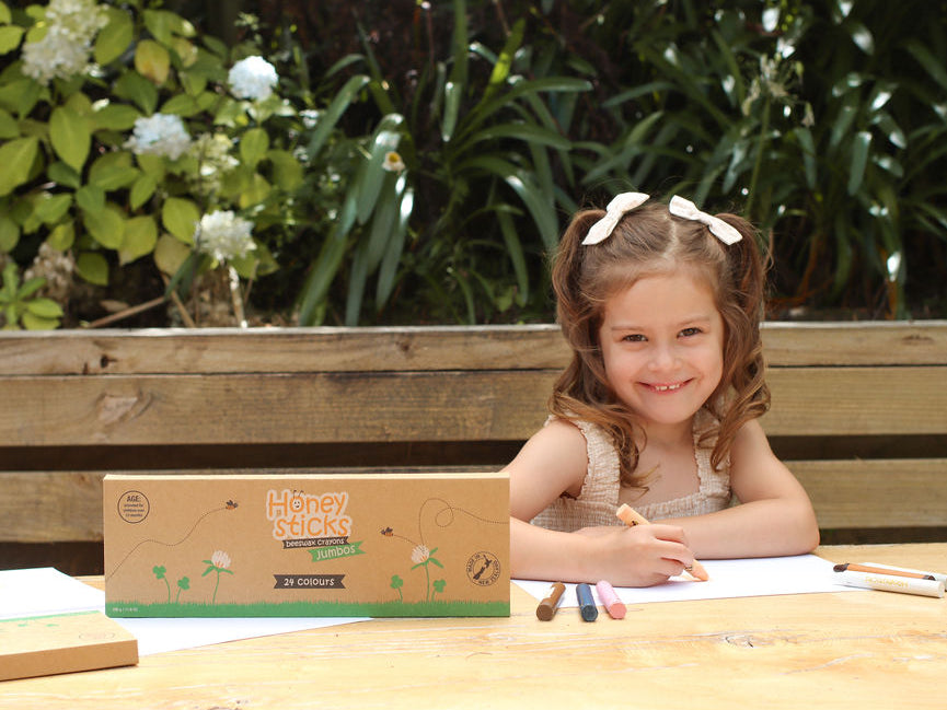 Young girl sitting at a table outdoors with a box of Honey Bunches of Oats in front of her.