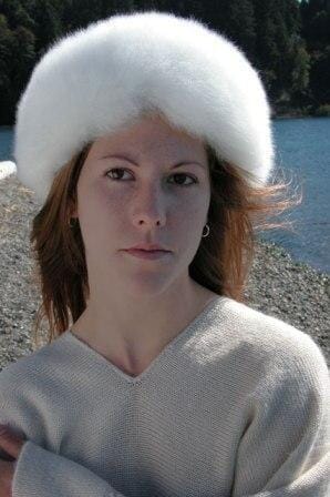 Person wearing a white fur hat and light sweater outdoors