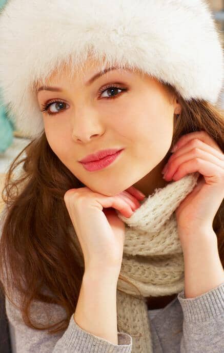 Woman wearing a white fur hat and gray sweater with a scarf, posing thoughtfully.
