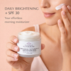 Person applying Glimmer Goddess Organic Vitamin C Moisturizer with SPF 30 on a beige background