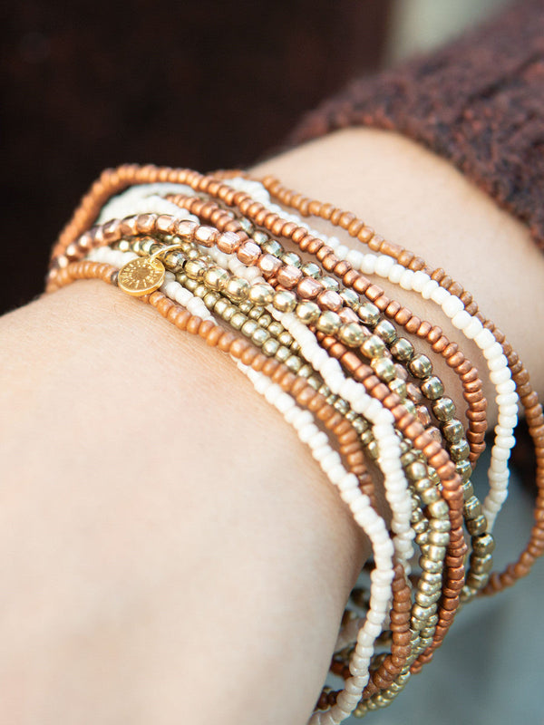 Gold and peach beaded bracelet set by Fair Anita laid flat, showing all 12 elastic bracelets