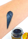 Dark shimmer balm swatch with blue glitter finish on a person's arm next to the Goth Girl 2 glass jar