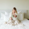 Woman holding a baby wrapped in a blanket on a bed with white pillows.