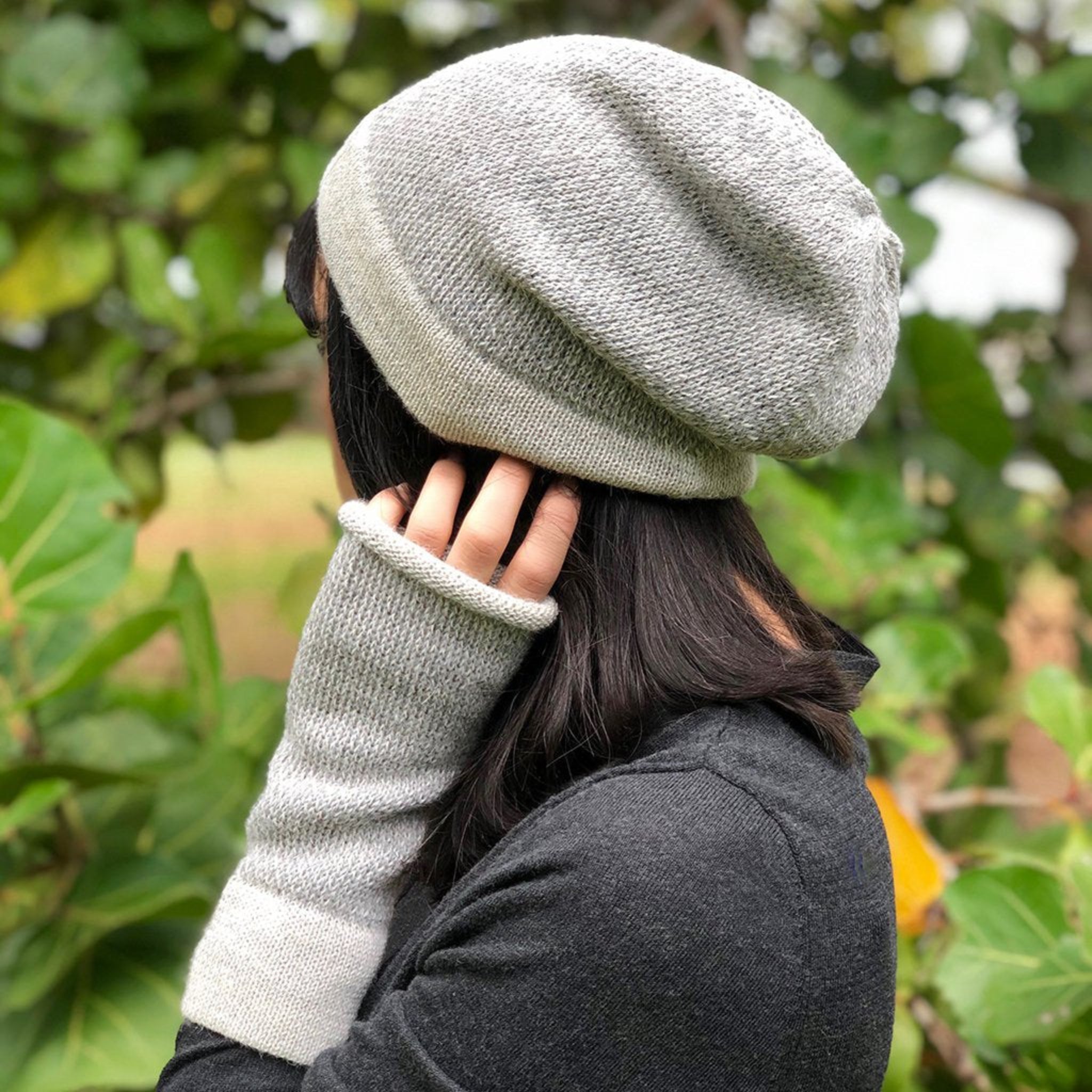 Person wearing a gray knit beanie and gloves in a natural setting