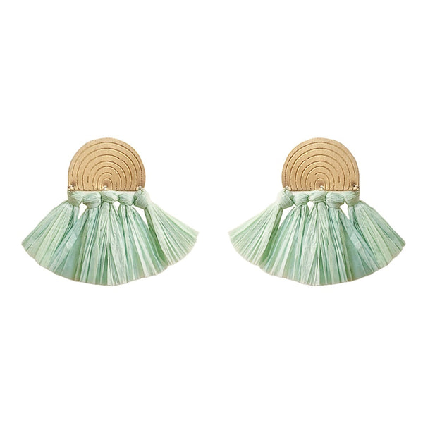 Pair of earrings with round beige tops and green tassel bottoms on a white background