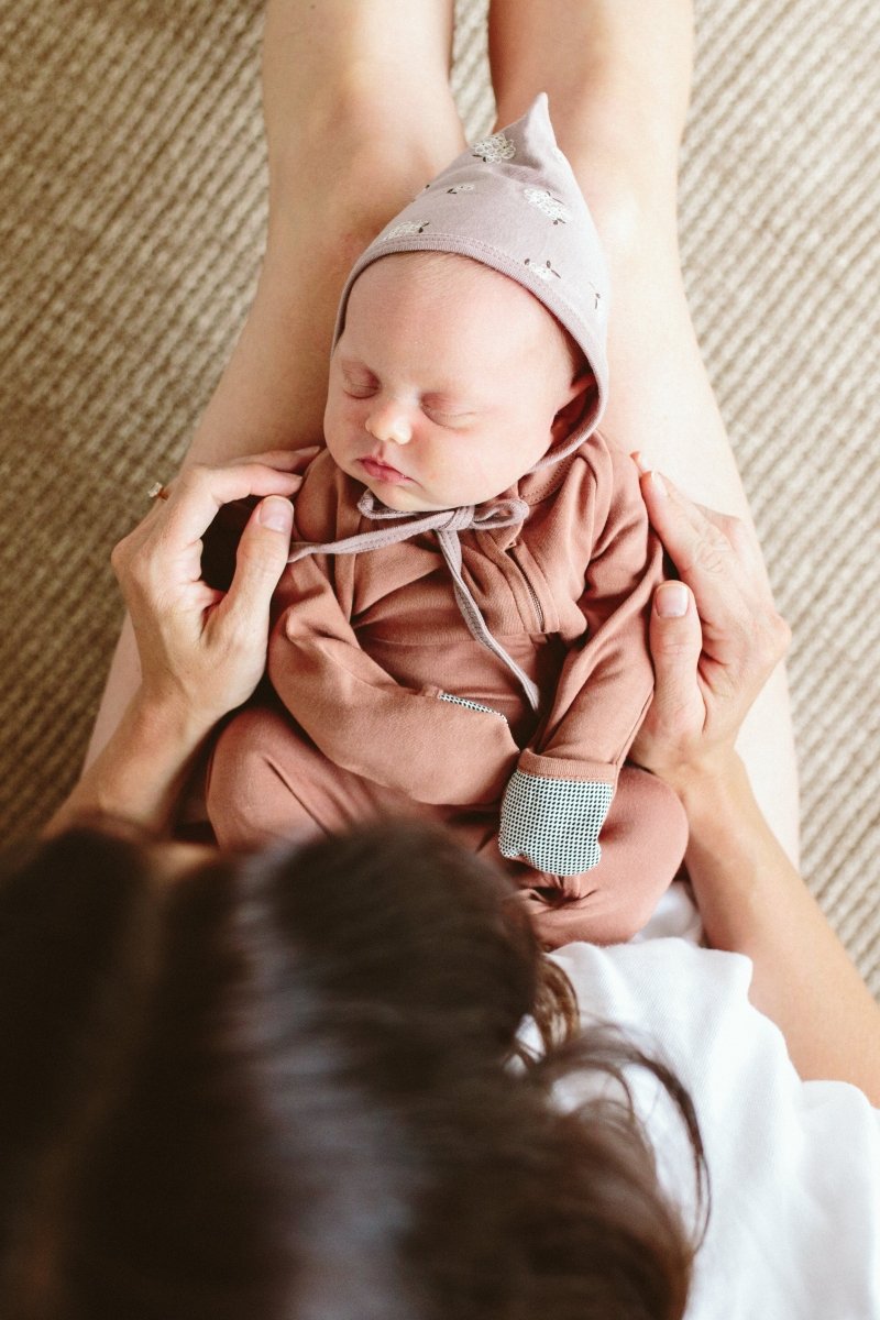Newborn baby in a pink outfit being held by a person on a textured surface