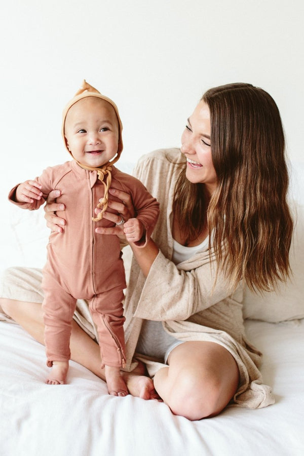 Woman holding a baby in a pink onesie on a white bed