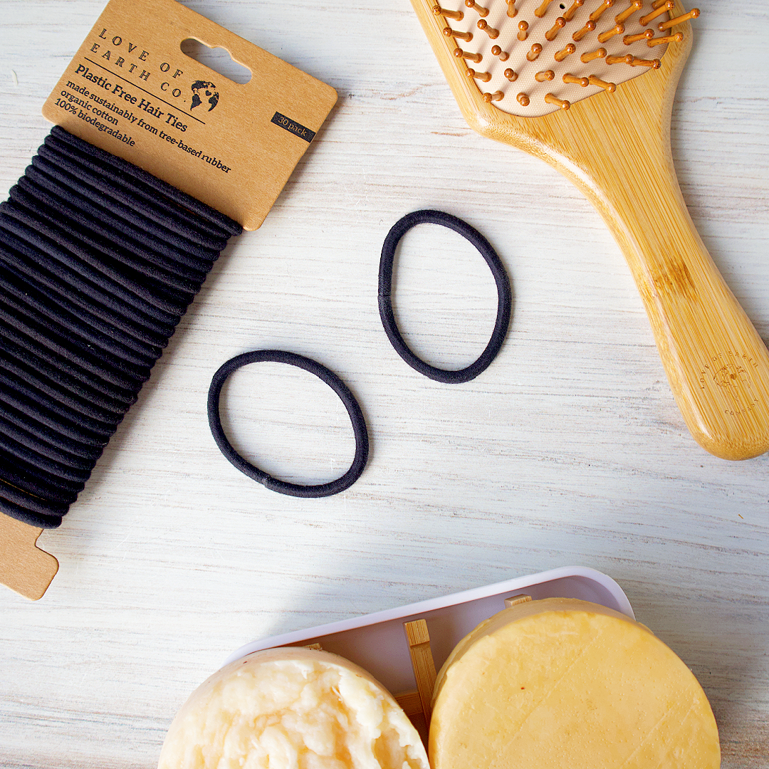 Bamboo hairbrush, black hair ties, and soap bars on a light wooden surface with 'Love of Earth Co.' packaging.