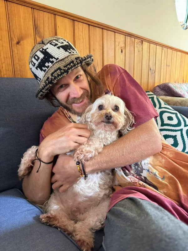 Man holding a small dog on a couch with a wooden panel wall in the background