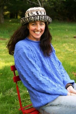 Woman wearing a blue sweater and patterned hat sitting on a red chair outdoors.