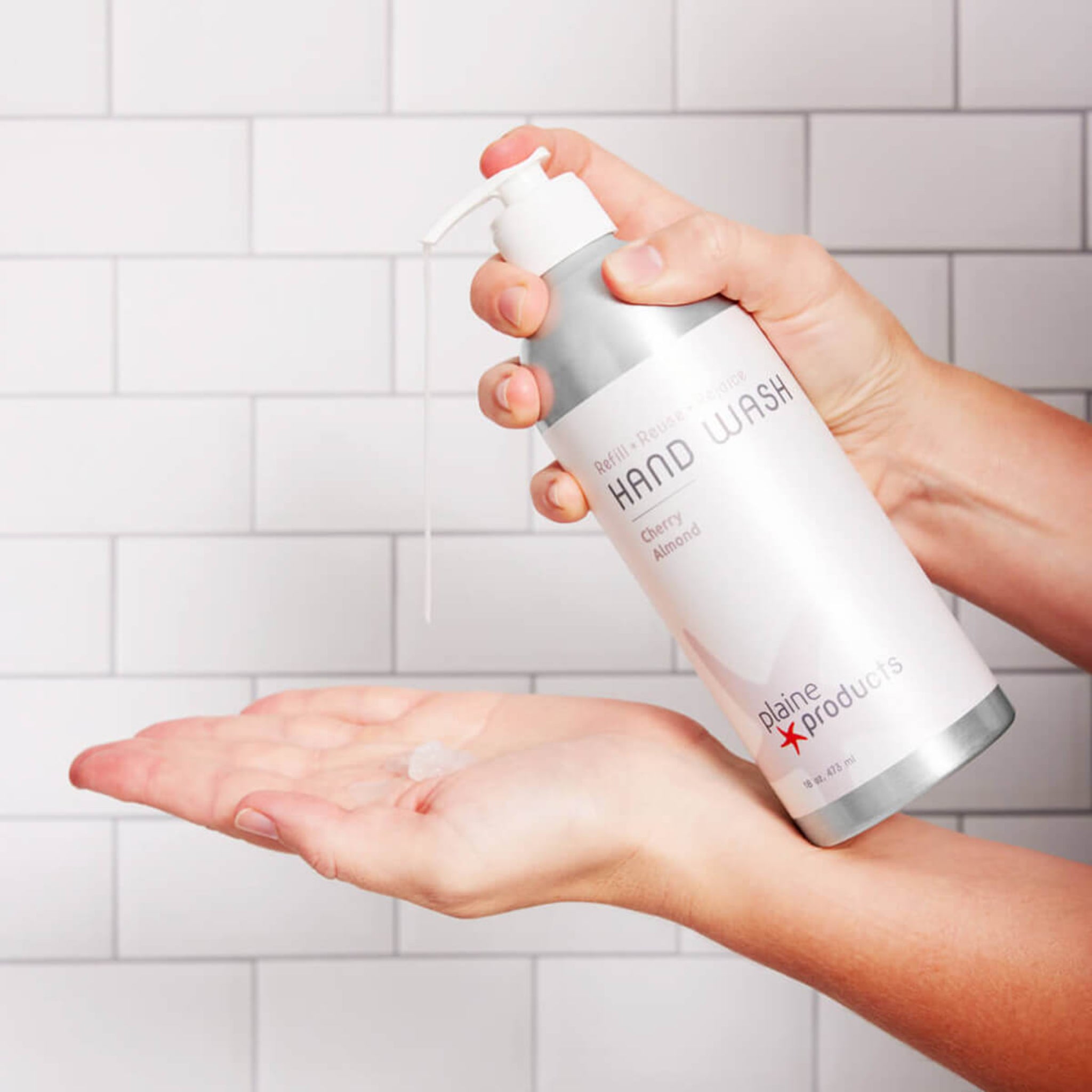 Hand holding a bottle of Colgate hand wash with soap on a tiled bathroom wall background