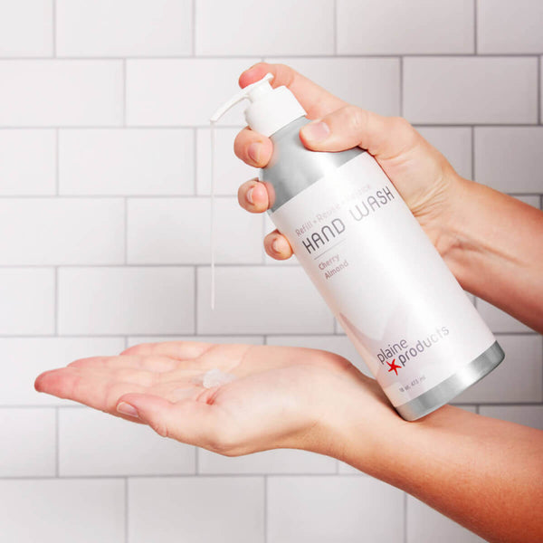 Hand holding a bottle of Colgate hand wash with soap on a tiled bathroom wall background