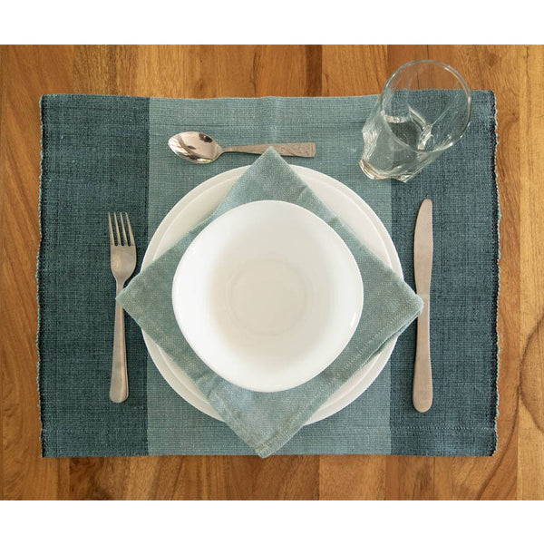 Set table with white plates, silverware, and a glass on a blue placemat.