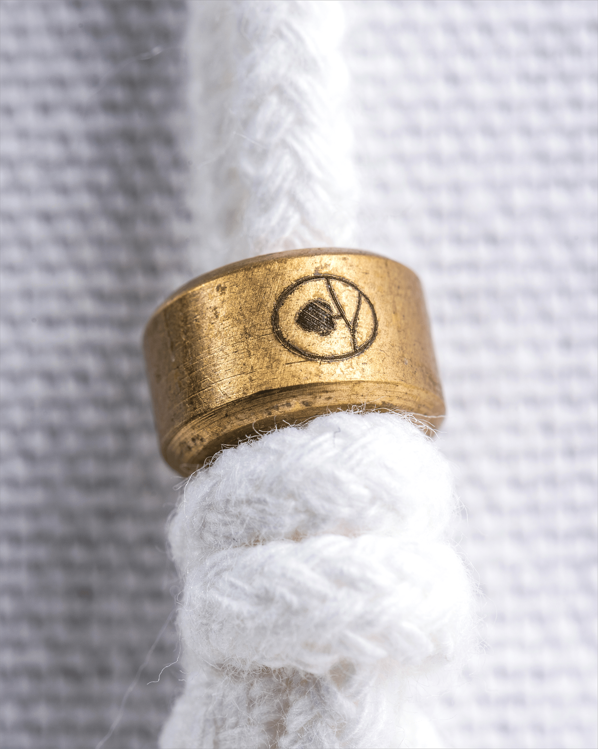 Gold ring with a symbol on a white rope against a textured gray background