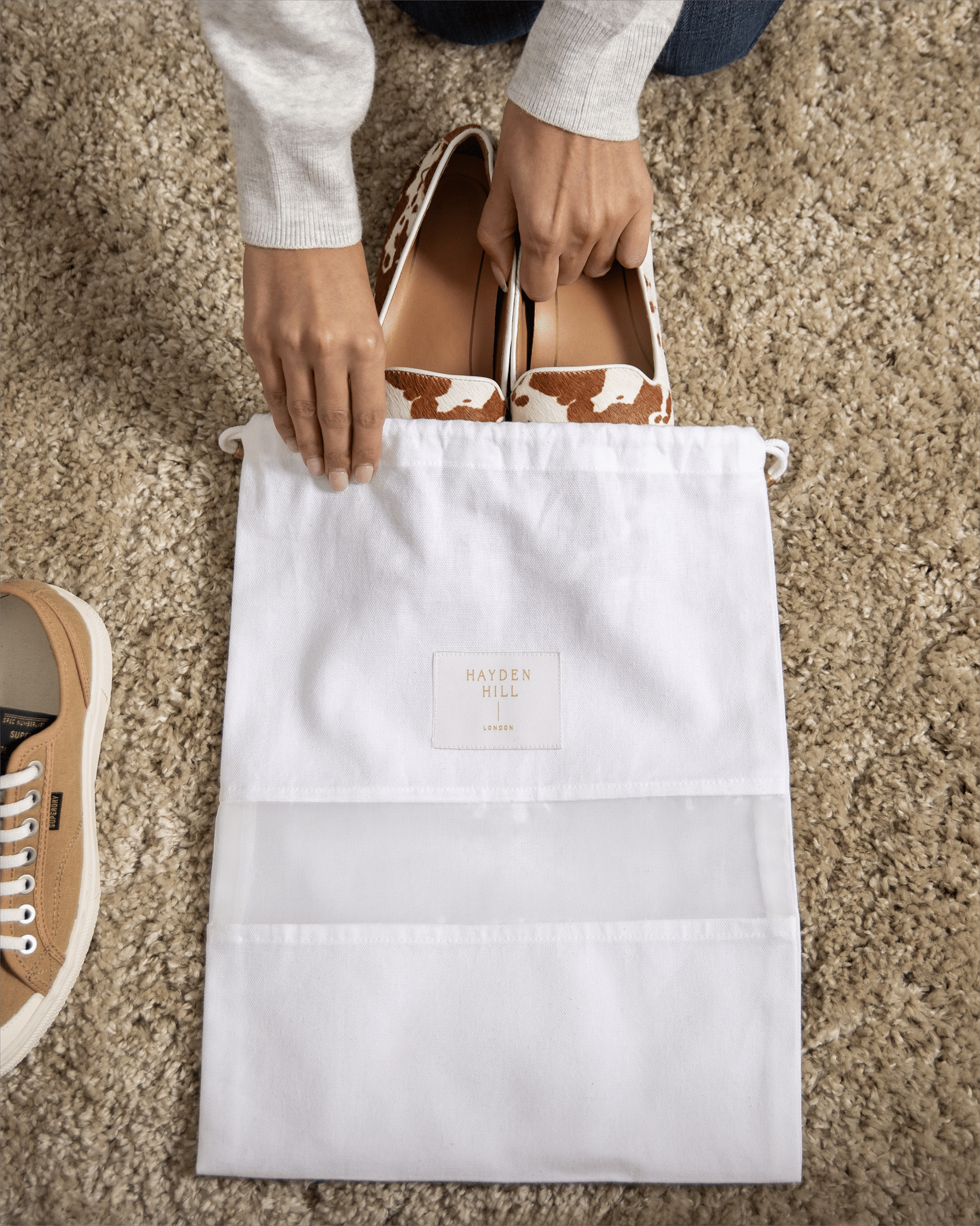 Bird's eye view of shoes being placed into a small Hayden Hill organic cotton dust bag