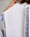 White jacket with 'Harden Hill' logo held by a person, hanging on a rack.
