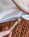 Close-up of a white pillow with a leather tag on a textured brown surface