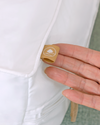 Close-up of a hand holding a small brown label on a white garment.