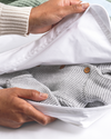 Person holding a white garment bag with a gray knit sweater inside.