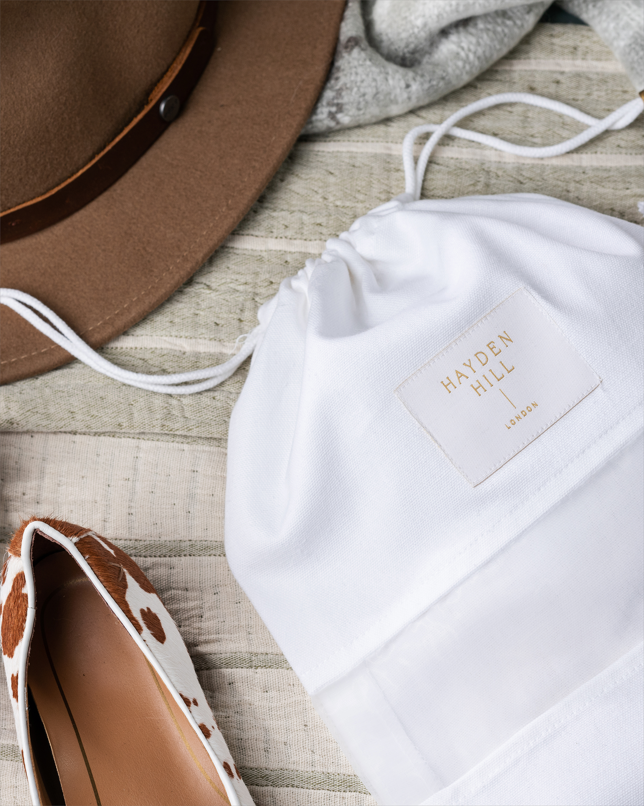 Set of 3 medium organic cotton dust bags by Hayden Hill styled on a bed with a hat and shoes