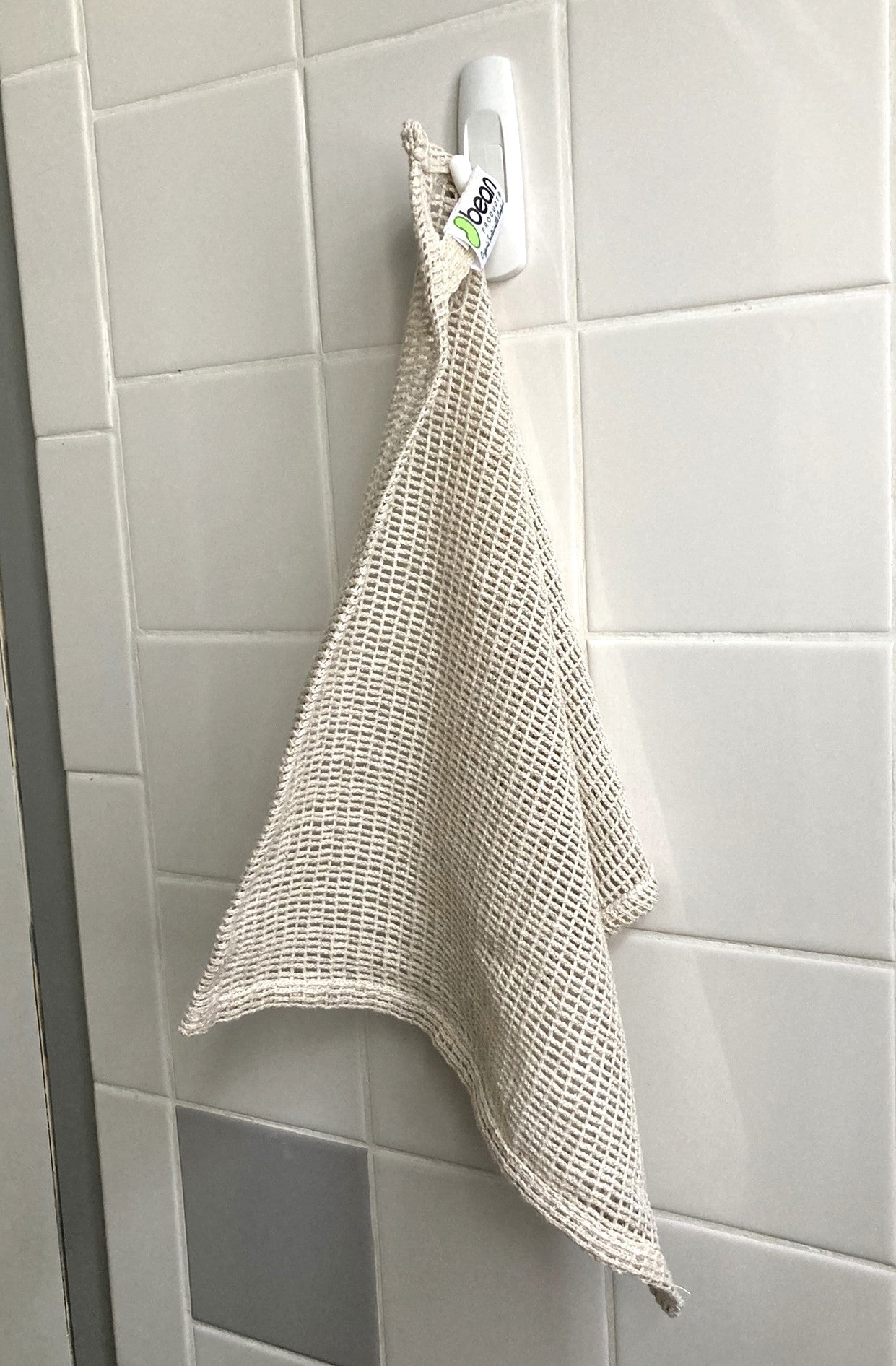 Textured beige towel hanging on a hook against a tiled wall.