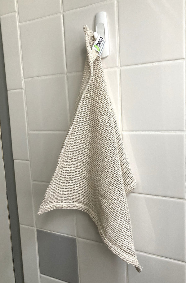 Textured beige towel hanging on a hook against a tiled wall.